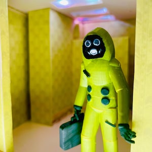 May include: A yellow hazmat suit figurine with a black gas mask and dark green gloves, holding a dark green briefcase. The figure stands in a room with yellow patterned walls and recessed ceiling lights that emit a soft blue glow.