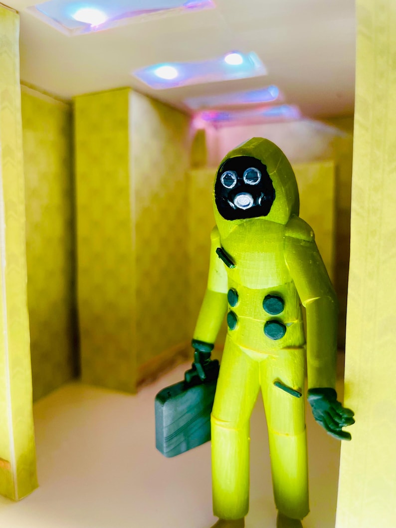 May include: A yellow hazmat suit figurine with a black gas mask and dark green gloves, holding a dark green briefcase. The figure stands in a room with yellow patterned walls and recessed ceiling lights that emit a soft blue glow.