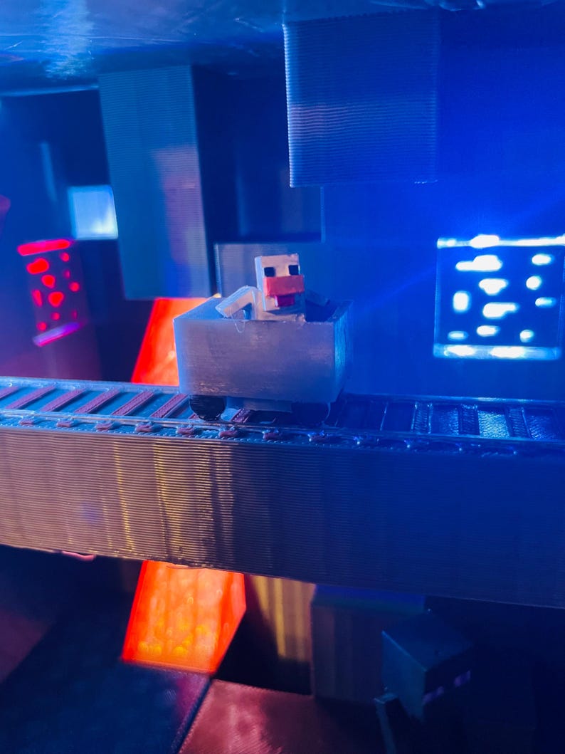 Puede incluir: Un personaje blanco de Minecraft montando un carro de mina azul en una v&iacute;a en una habitaci&oacute;n iluminada en azul y rojo. El personaje tiene la nariz rosa y lleva una camisa blanca.
