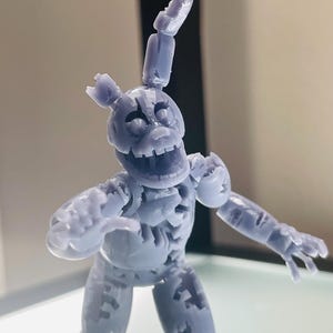 May include: A light gray, 3D-printed articulated figure of a rabbit-like character with a damaged, weathered appearance. The figure features a wide, open-mouthed expression, one long upright ear, and one broken ear, with visible segmented joints on the limbs.