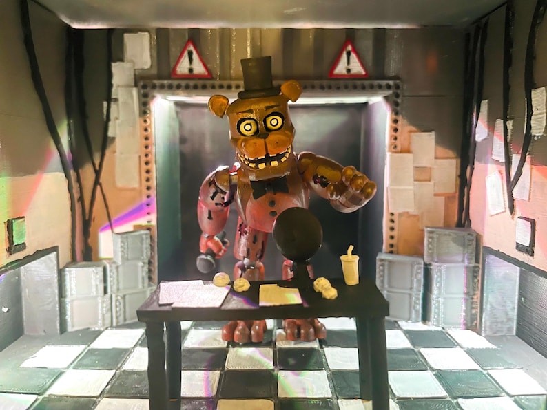 May include: A brown animatronic bear figure with a black top hat and bowtie stands behind a black desk. The figure has glowing yellow eyes, a wide mouth with visible teeth, and distressed brown plating. The desk holds papers and a cup.