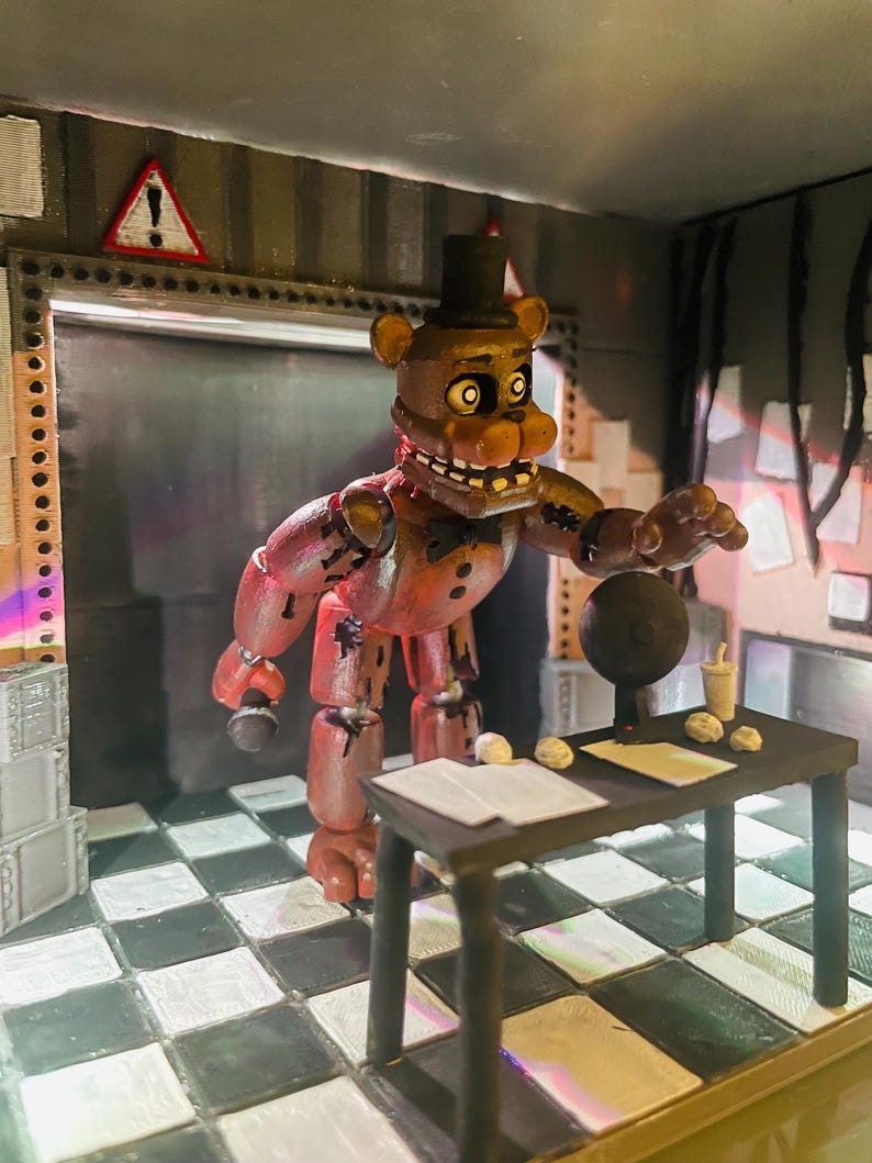 May include: A brown bear animatronic figure wearing a black top hat and bowtie, holding a microphone. The figure stands in a room with a black and white chequered floor, a black desk with papers, a small cup, and a circular object, with a warning sign.
