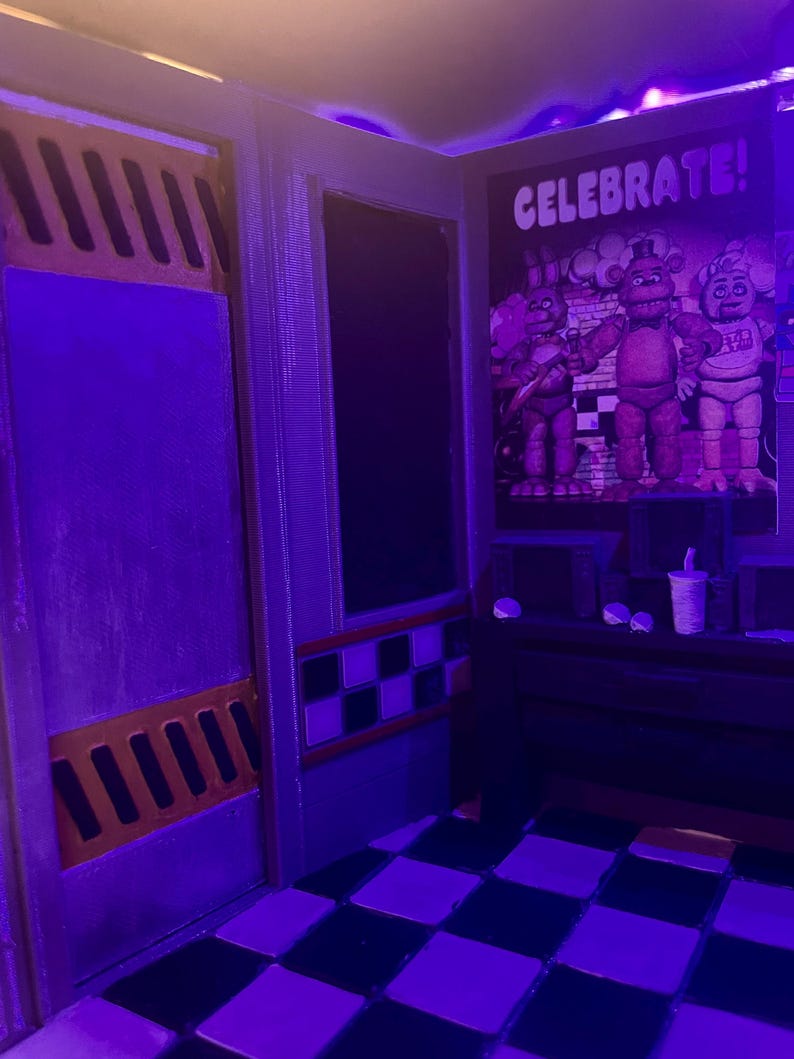 K&ouml;nnte beinhalten: Ein Miniatur-Diorama eines Sicherheitsb&uuml;ros mit schwarz-wei&szlig; kariertem Boden, einer Wand mit einem Poster von drei Animatronic-Figuren und dem Text CELEBRATE!, einer dunklen T&uuml;r mit orangefarbenen L&uuml;ftungsschlitzen und violetter Beleuchtung.
