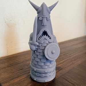 Op de afbeelding: Een lichtpaars 3D-geprint beeldje van een krijger met een gehoornde helm, die een zwaard in de rechterhand en een rond schild in de linkerhand houdt. Het figuur heeft een getextureerde, schubachtige romp, een wijd open mond en een voetstuk.
