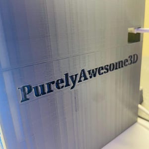 Puede incluir: Una caja gris impresa en 3D con el texto "PurelyAwesome3D" impreso en el lateral.