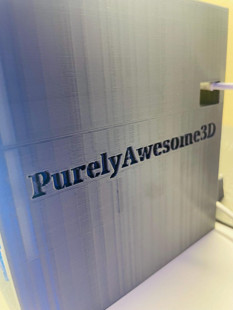 Puede incluir: Una caja gris impresa en 3D con el texto "PurelyAwesome3D" impreso en el lateral.
