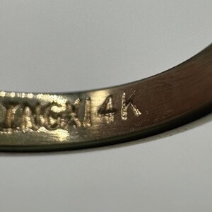 May include: Close-up of a gold ring with the inscription "INGAI 14K" engraved on the inside. The ring is a warm gold color and appears to be well-worn.