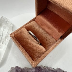 May include: A simple silver band ring in a peach velvet ring box.