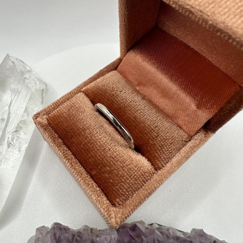 May include: A simple silver band ring in a peach velvet ring box.