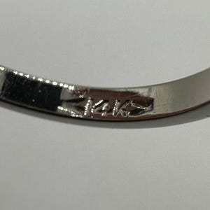 May include: Close-up of a silver band with the inscription "14K" on the inside.