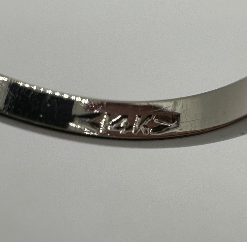 May include: Close-up of a silver band with the inscription "14K" on the inside.