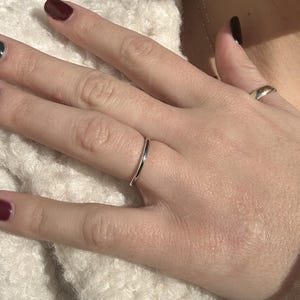 May include: A thin silver band ring on a finger.