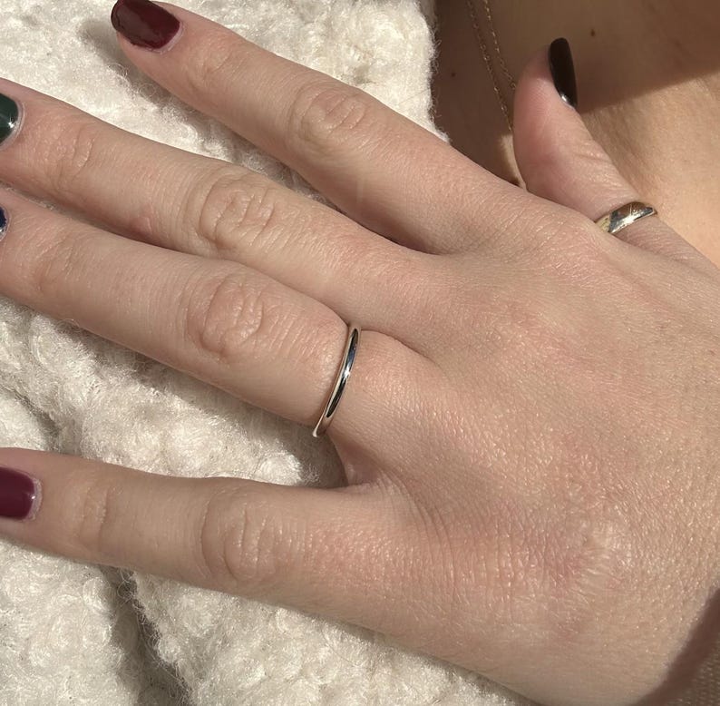 May include: A thin silver band ring on a finger.