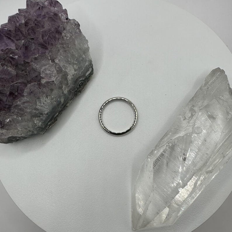 May include: A silver ring with a textured surface, displayed on a white background with two crystals.