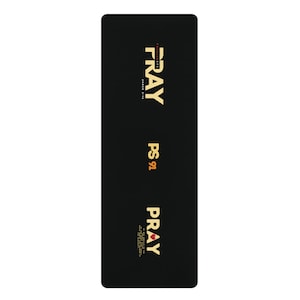 Puede incluir: Estera de yoga negra con las palabras "Pray" y "PS 91" en letras doradas. La palabra "Pray" se repite en la parte inferior con un corazón rojo.