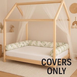 Puede incluir: Una cama con estructura de madera clara en forma de casa, con un colchón blanco y almohadas cilíndricas con estampado de hojas verdes. Tela blanca transparente cuelga del marco. El texto "COVERS ONLY" se muestra abajo a la derecha.