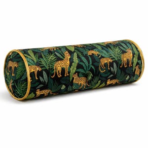 May include: A cylindrical cushion with a black background featuring a jungle scene with green leaves and yellow cheetahs. The cushion has a gold trim.