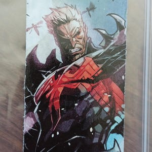 May include: Comic book trading card featuring a stern-faced, muscular character with white hair and a black and red costume. The character is in a dynamic pose, with a detailed illustration style. The background is a light blue with dark shapes.