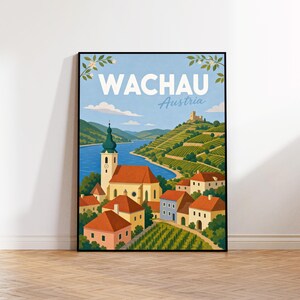 Peut inclure: Une affiche de voyage encadrée représentant une illustration paysagère de la région de la Wachau en Autriche. L'œuvre montre un village avec une église, des bâtiments aux toits rouges, des vignobles en terrasses et une rivière sous un ciel bleu.