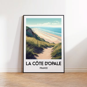 Op de afbeelding: Een poster met een schilderachtig uitzicht op een strand in Frankrijk. De poster toont een pad dat een grasbegroeide heuvel afdaalt naar een zandstrand met blauw water en een bewolkte lucht. De tekst "LA CÔTE D'OPALE" en "FRANCE" staat onderaan de poster gedrukt.