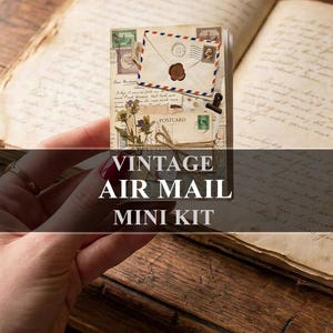 May include: A small rectangular paper kit featuring a vintage air mail theme with an envelope graphic, a wax seal, a postcard, and dried flower illustrations. The kit includes the text VINTAGE AIR MAIL MINI KIT printed in white over the center.