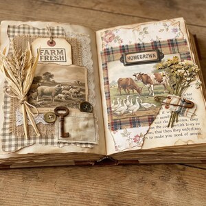 May include: Open vintage book with collaged pages. One page features a "FARM FRESH" tag, a sheep illustration, a key, and buttons. The other page has a "HOMEGROWN" label, a cow and geese illustration, and dried flowers.