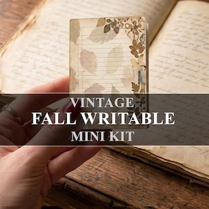 May include: A small rectangular notepad featuring horizontal lines and a decorative border of pressed autumn leaves in shades of brown, tan, and muted green. The paper has an aged, parchment-like appearance with a soft, neutral color palette.
