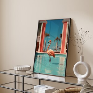 May include: A framed print of a pink flamingo standing in a blue pool with a pink and white building in the background.