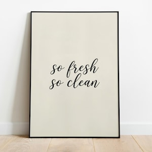May include: A rectangular wall art print featuring a cream-coloured background and a thin black frame. The text "so fresh so clean" is printed in the centre in a black, cursive script font, arranged in two lines with the words stacked vertically.