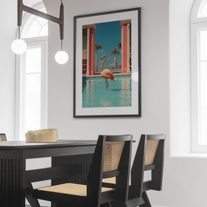 May include: A black framed print of a pink flamingo standing in a blue pool with a pink building in the background.