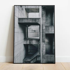 May include: A black and white framed wall art print featuring a perspective view of a brutalist concrete structure with geometric levels, sharp rectangular openings, and deep shadows cast across the weathered, textured gray surfaces.