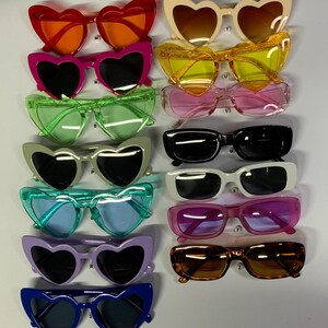 May include: A set of 12 pairs of heart-shaped sunglasses in various colors, including red, orange, pink, yellow, green, blue, purple, and black. The sunglasses have a retro style and are perfect for adding a touch of fun to any outfit.