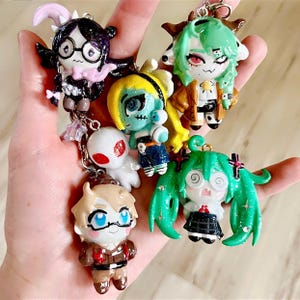 May include: A collection of five small, glittery, hand-painted character charms attached to a metal keychain. The figures include a dark-haired character with glasses, a green-haired horned figure, a yellow-haired figure, a white ghost, and a green-haired figure with twin tails.
