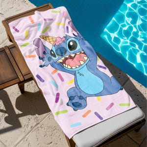 May include: A pink beach towel with a blue Stitch character from Lilo & Stitch. Stitch is wearing an ice cream cone on his head and has a happy expression. The towel has a sprinkle pattern in various colors.