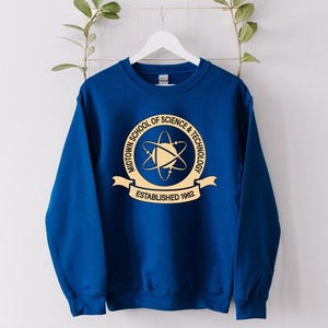 May include: A royal blue sweatshirt with a gold emblem featuring the text "MIDTOWN SCHOOL OF SCIENCE & TECHNOLOGY" and "ESTABLISHED 1962". The emblem includes a stylized atom symbol. The sweatshirt is hanging on a white hanger.