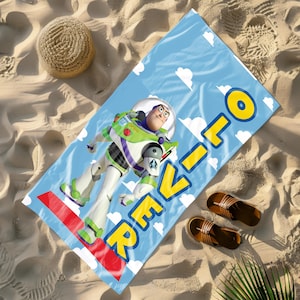 May include: A blue beach towel with a cartoon image of Buzz Lightyear from Toy Story. The towel has the text "REVILO" in yellow letters on it.