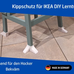 Könnte beinhalten: Ein hellblauer Holzhocker mit weißen, aus Kunststoff gefertigten Kippschutzfüßen. Der Hocker trägt den Aufdruck "Kippschutz für IKEA DIY Lernturm" und "Passend für den Hocker Bekväm". Der Text "MADE IN GERMANY" ist auf einer kleinen deutschen Flagge aufgedruckt.