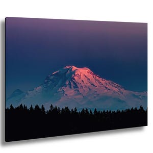 May include: A landscape print featuring a snow-capped mountain illuminated by a pink and red sunset. The mountain is set against a dark blue and purple sky, with a silhouetted forest in the foreground.