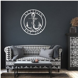 May include: A white metal anchor with rope design and the text "Allison Est. 2021" in a circle, mounted on a dark gray wall above a black and white patterned sofa.