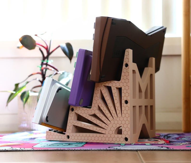 K&ouml;nnte beinhalten: Ein beigefarbener Plastikst&auml;nder mit einem Wabenmuster und einem Sonnenstrahl-Design h&auml;lt eine Sammlung von Videospielkassetten. Die Kassetten sind lila, grau und braun.