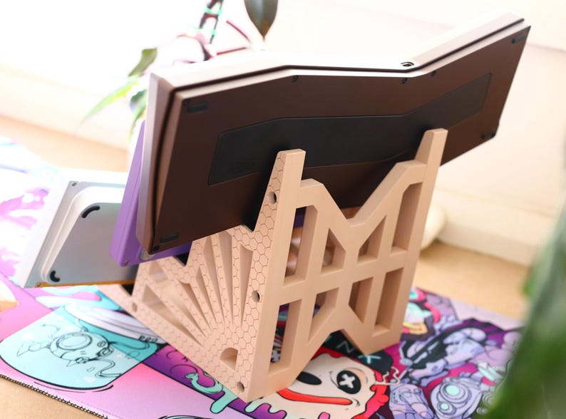 K&ouml;nnte beinhalten: Ein beigefarbener Plastikst&auml;nder mit geometrischem Design h&auml;lt eine braune Tastatur. Die Tastatur ist nach oben geneigt und der St&auml;nder steht auf einer bunten Oberfl&auml;che mit einem Cartoon-Design.