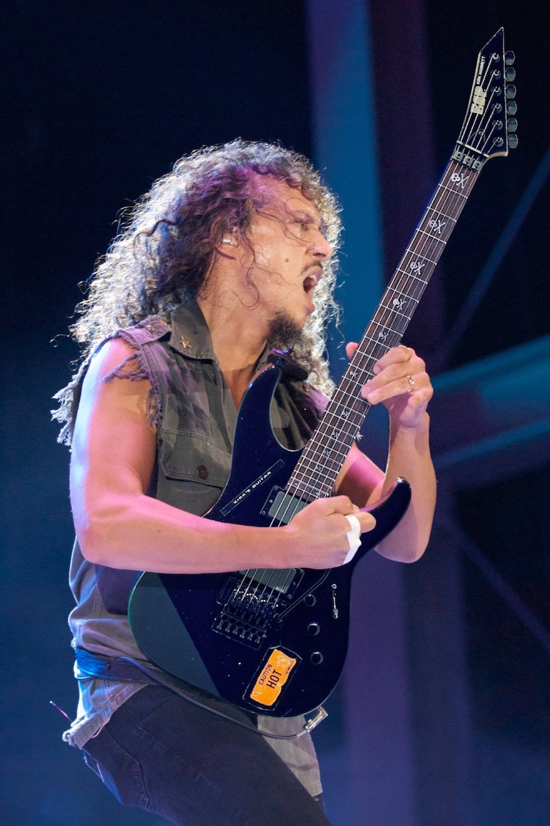 Może przedstawiać: Mężczyzna gra na czarnej gitarze elektrycznej z białym pickguadem. Gitara ma na korpusie czarno-biały motyw czaszki i napis "Kirk's Guitar". Gitara ma r&oacute;wnież naklejkę z napisem "Dunlop HOT".