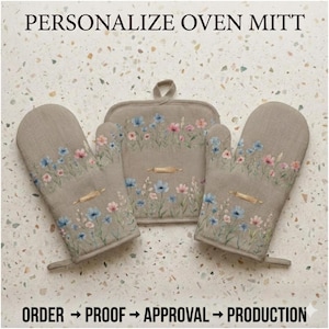 May include: A set of personalized oven mitts and a pot holder. The beige mitts and pot holder are decorated with a floral design in blue and pink, and a rolling pin. The text "PERSONALIZE OVEN MITT" is at the top.