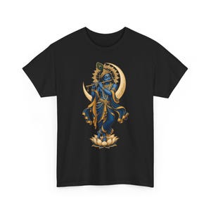 Könnte beinhalten: Ein schwarzes T-Shirt mit einem Grafikdruck einer blauhäutigen Figur, die Flöte spielt und auf einer Lotusblume steht. Die Figur trägt goldenen Schmuck und eine Pfauenfeder vor einem großen goldenen Halbmond und einem Heiligenschein.