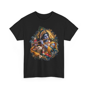 Könnte beinhalten: Ein schwarzes Kurzarm-T-Shirt mit einem farbenfrohen Grafikdruck einer blauhäutigen Figur, die eine goldene Flöte spielt, geschmückt mit Schmuck und einer Pfauenfedernkrone, begleitet von einem kleinen weißen Kalb inmitten von Blumen- und Pfauenfedermotiven.