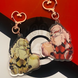 Puede incluir: Dos llaveros con ilustraciones de dibujos animados de un perro blanco y rojo con marcas negras. Los llaveros están hechos de acrílico transparente y tienen cierres en forma de corazón de color dorado.