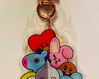 May include: A clear acrylic keychain with a rose gold star-shaped clasp. The keychain features a group of seven cartoon characters, including a red heart, a pink bunny, a blue dog, a purple and white character with an X and O on its face, a yellow character with a tongue sticking out, a blue koala, and a white fluffy character. The characters are surrounded by gold glitter.