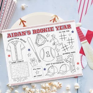 May include: A baseball-themed activity sheet with the text "AIDAN'S ROOKIE YEAR" in red. The sheet includes a jersey design, baseball bat, glove, ball, and various games like tic-tac-toe and a word search. The sheet is decorated with baseball stitching.
