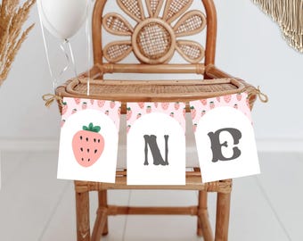 Puede incluir: Una pancarta rosa y blanca con fresas y la palabra "ONE" en letras negras. La pancarta está atada a una silla alta de mimbre.