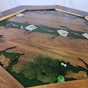 Op de afbeelding: Een op maat gemaakte achthoekige pokertafel met een donkere houten afwerking en een groen rivierontwerp. De tafel heeft speelkaarten, pokerchips en dobbelstenen. De afmetingen van de tafel zijn niet zichtbaar.